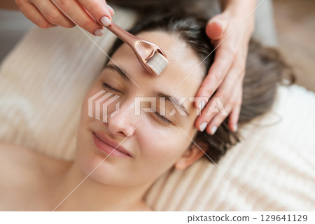 Microneedle mesotherapy in cosmetology salon, close up of face of a girl client. Roller with micro needles used for stimulation of skin regeneration and introduction of various rejuvenating drugs 129641129