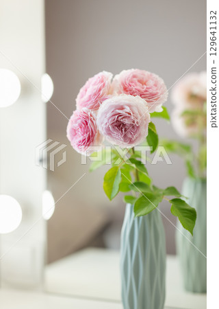 Beautiful tender pink flowers in a light blue vase near the mirror, close up. Interior design of beauty salon in white and pastel colours Beautiful tender pink flowers in a light blue vase near the mirror, close up. Interior design of beauty salon in white and pastel colours 129641132