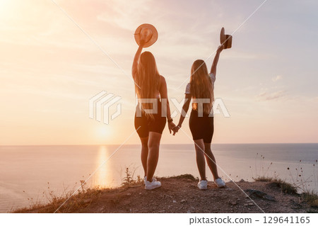 Silhouettes of Two Women Holding Hands and Gazing at the Sunset Silhouettes of Two Women Holding Hands and Gazing at the Sunset 129641165