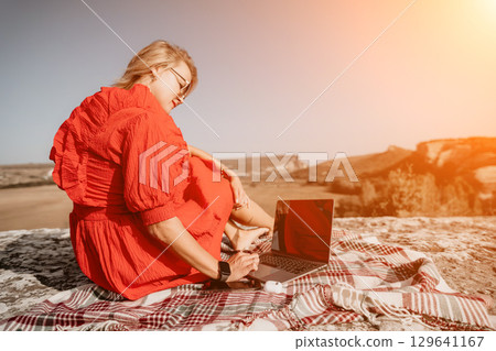 Young Woman in Red Dress Using Laptop on a Mountaintop Young Woman in Red Dress Using Laptop on a Mountaintop 129641167