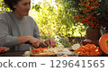 Woman preparing Thanksgiving meal in outdoor kitchen, skillfully chopping vegetables, surrounded by colorful fall foliage, creating a warm and festive atmosphere for celebration 129641565
