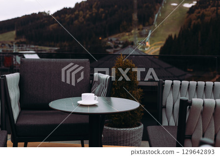 A cup of coffee, tea on a table and scenic mountain view. A tranquil scene of hotel terrace, rooftop with mountain backdrop. Relaxation, leisure scene 129642893
