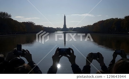 Tourists photographing monument reflected in a calm lake on a sunny day 129643944