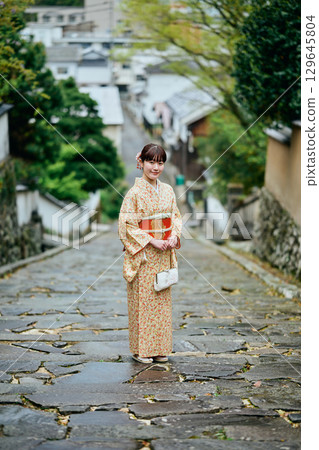 A woman in a kimono walking down a cobblestone slope 129645804