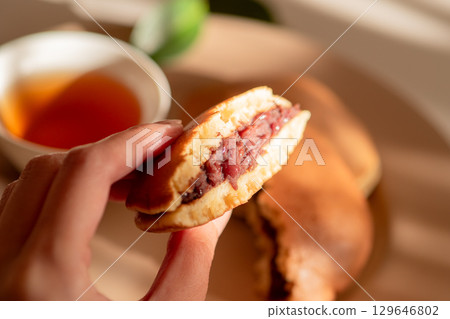 A close-up of a dorayaki being held in the hand. It is filled with plenty of bean paste. 129646802