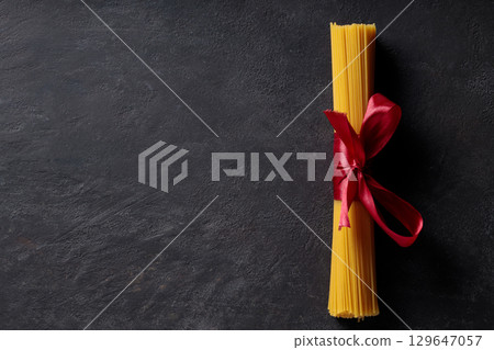 Raw Spaghetti Bundle Tied with Red Ribbon on Dark Background Top View Copy Space Raw Spaghetti Bundle Tied with Red Ribbon on Dark Background Top View Copy Space 129647057