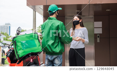 Asian deliveryman by motorbike give pizza in paper box to female customer 129648045