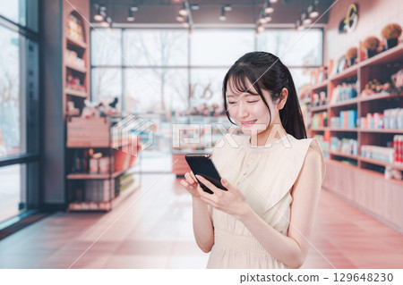 一位年輕女子在購物時用智慧型手機搜索 一位年輕女子在購物時用智慧型手機搜索 129648230