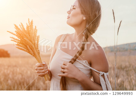 Woman wheat field. Agronomist, Woman farmer check golden ripe barley spikes in cultivated field. A woman is holding a bunch of wheat in her arms. 129649993