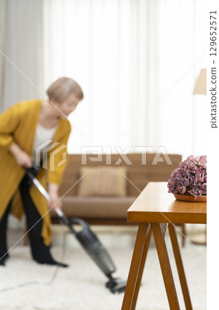 Senior woman vacuuming in the living room 129652571