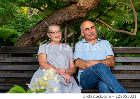 Elderly couple sitting on bench enjoying nature together 129653321
