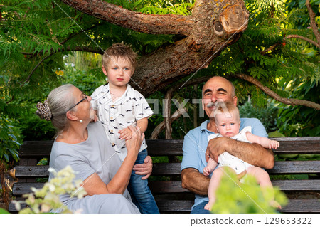 Grandparents with young grandchildren sitting on park bench Grandparents with young grandchildren sitting on park bench 129653322