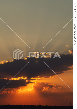 Sunset with radiant sun rays piercing dark clouds near horizon Sunset with radiant sun rays piercing dark clouds near horizon 129653323
