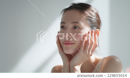 一位美麗的日本女性，裸露著皮膚，手托著臉頰，站在白色的牆壁前 129655014