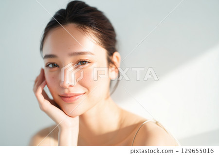 一位美麗的日本女性，裸露著皮膚，手托著臉頰，站在白色的牆壁前 129655016