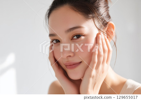 一位美麗的日本女性，裸露著皮膚，手托著臉頰，站在白色的牆壁前 129655017