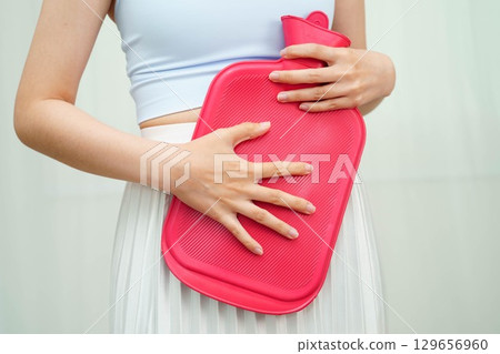 Woman using hot water bottle to relieve menstrual abdominal pain. Woman using hot water bottle to relieve menstrual abdominal pain. 129656960
