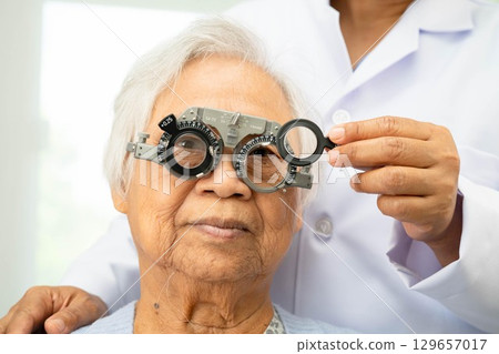 Optometrist checking Asian elderly woman ophthalmic vision eye test and using optical trial frame. Optometrist checking Asian elderly woman ophthalmic vision eye test and using optical trial frame. 129657017