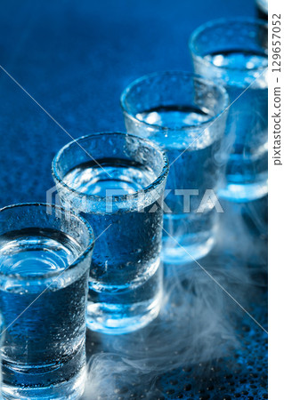 Wet glasses of vodka in smoke on dark blue background. 129657052