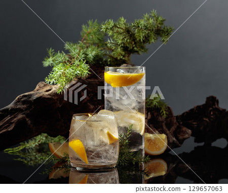 Hard seltzer with ice and lemon on a black reflective background. 129657063