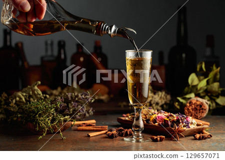 Yellow herbal liquor or mixture is poured from a vintage bottle into a glass. 129657071