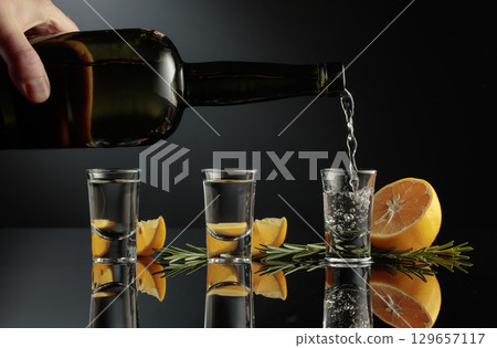 Gin with lemon and rosemary on a black reflective background. 129657117