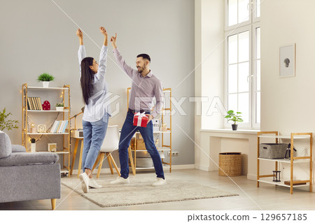 Young happy man and woman having fun standing with present gift box at home. 129657185