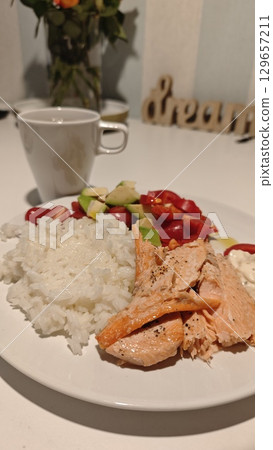 Grilled salmon served with white rice, avocado salad, and a cup of tea on a clean white table Grilled salmon served with white rice, avocado salad, and a cup of tea on a clean white table 129657211