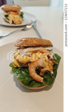 Shrimp and egg sandwich on a sesame bagel with fresh lettuce served on a white plate Shrimp and egg sandwich on a sesame bagel with fresh lettuce served on a white plate 129657212