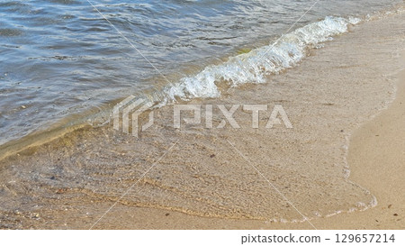 Gentle sea wave rolling onto a sandy beach under bright sunlight. The image captures tranquility, relaxation, and the natural rhythm of ocean life Gentle sea wave rolling onto a sandy beach under bright sunlight. The image captures tranquility, relaxation, and the natural rhythm of ocean life 129657214