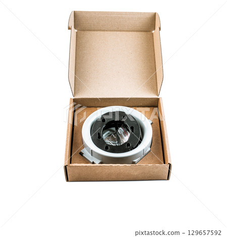 Round ceiling light fixture housing with black inner ring, presented inside open craft cardboard box, accessory for recessed installation work. Round ceiling light fixture housing with black inner ring, presented inside open craft cardboard box, accessory for recessed installation work. 129657592