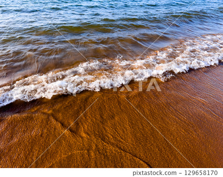 Serene shoreline with gentle waves meeting sandy beach Serene shoreline with gentle waves meeting sandy beach 129658170