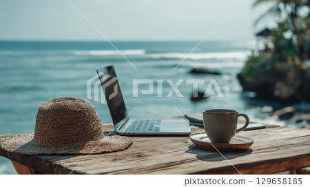 Remote work setup with laptop, coffee, and hat on a wooden table by the ocean Remote work setup with laptop, coffee, and hat on a wooden table by the ocean 129658185
