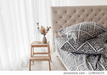 Modern geometric black and white bedding with stacked pillows in bright bedroom interior 129658235