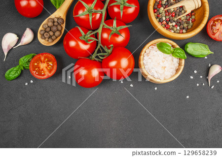 Fresh ripe tomatoes on the vine with garlic cloves, basil leaves, pink Himalayan salt, whole allspice, and a bowl of colorful peppercorns on a dark stone background, top view. copy space Fresh ripe tomatoes on the vine with garlic cloves, basil leaves, pink Himalayan salt, whole allspice, and a bowl of colorful peppercorns on a dark stone background, top view. copy space 129658239