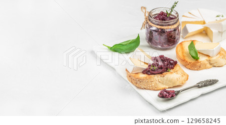 Brie cheese with caramelized red onion jam on toasted sesame bread slices, served with fresh basil, a jar of onion chutney, and a spoon, on a white marble board with copy space Brie cheese with caramelized red onion jam on toasted sesame bread slices, served with fresh basil, a jar of onion chutney, and a spoon, on a white marble board with copy space 129658245