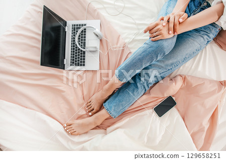 Relaxed remote work setup with laptop, headphones, and smartphone on bed Relaxed remote work setup with laptop, headphones, and smartphone on bed 129658251