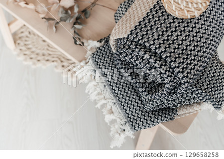 Cozy folded knitted blanket with fringes on a wooden bench 129658258