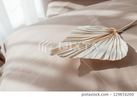 Dried palm leaf decor on beige bed linen in soft sunlight Dried palm leaf decor on beige bed linen in soft sunlight 129658260