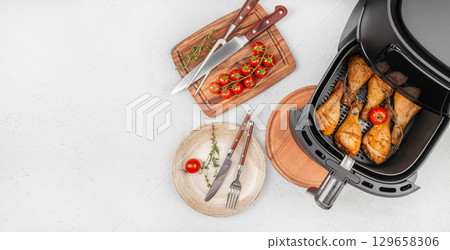 Air fryer chicken drumsticks with fresh tomatoes and herbs on a modern kitchen countertop. top view. copy space 129658306