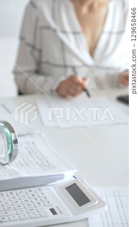Group of accountants are working together, using a magnifying glass and a calculator, to audit financial reports in office. Audit and taxes in business 129658466