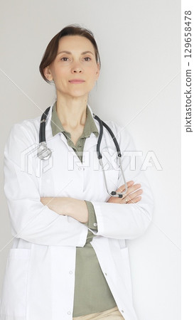 Female medical professional in white lab coat, stethoscope draped, standing with crossed arms and displaying confident, authoritative healthcare demeanor. Medicine and health care 129658478