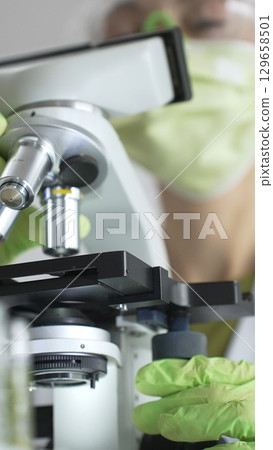 Close up of green gloved hands of a scientist adjusting a microscope in a laboratory, emphasizing the significance of scientific research and analysis. Medicine, healthcare and science concept Close up of green gloved hands of a scientist adjusting a microscope in a laboratory, emphasizing the significance of scientific research and analysis. Medicine, healthcare and science concept 129658501
