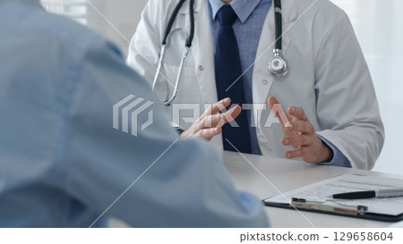 Medical professional explaining diagnosis, gesturing hands to patient during consultation in well lit clinical setting. Medicine and health care concept 129658604