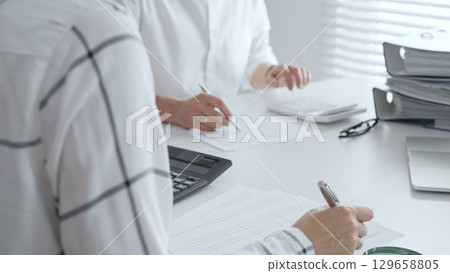 Unrecognizable accountants working together in a well lit office, analyzing financial data and preparing reports with calculators and pens. Audit and taxes in business Unrecognizable accountants working together in a well lit office, analyzing financial data and preparing reports with calculators and pens. Audit and taxes in business 129658805