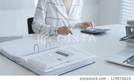 Calculator on financial documents, with an accountant taking notes, emphasizing accounting, finance, and tax preparation, close up. Audit and taxes in business 129658828