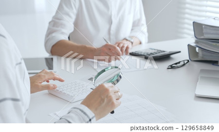 Team of accountants collaborating on financial analysis, using a magnifying glass, calculator, and laptop to ensure data accuracy. Audit and taxes 129658849