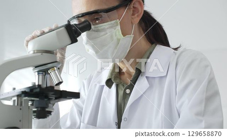 Female scientist examining microscope slide, wearing protective gear while conducting medical research in sterile laboratory environment. Medicine, healthcare and science concept 129658870