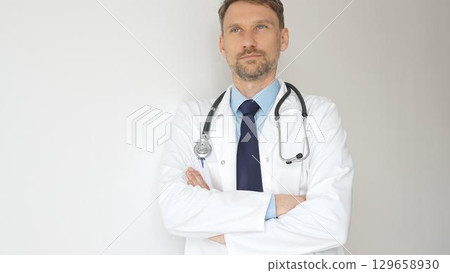Headshot of a confident doctor man wearing stethoscope and white coat, is standing with crossed arms, representing medical professionalism and expertise. Medicine and health care 129658930