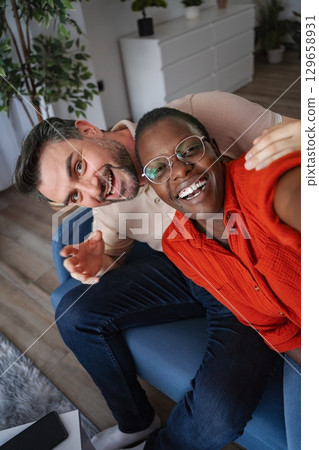 Happy couple taking a selfie while sitting on the couch at home Happy couple taking a selfie while sitting on the couch at home 129658931